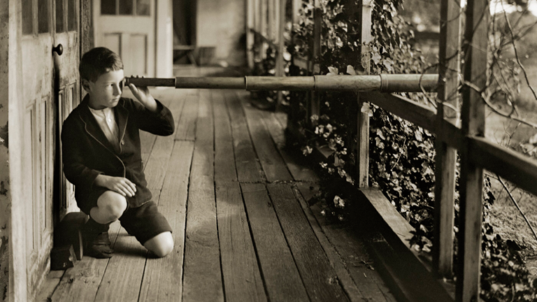 Boy on a wooden verandah looking through a telescope.